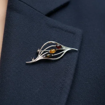 Srebrna broszka w kształcie listka z trzema małymi bursztynami na marynarce
