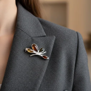 Elegancka srebrna broszka z kolorowym bursztynem przypięta do marynarki damskiej.