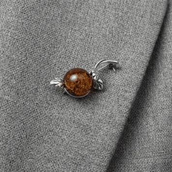 Elegancka srebrna broszka z okrągłym bursztynem przypięta do szarej marynarki